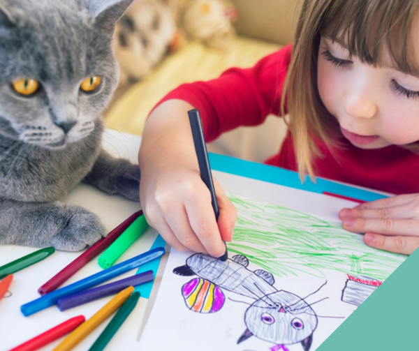 A little girl drawing with a cat by her side