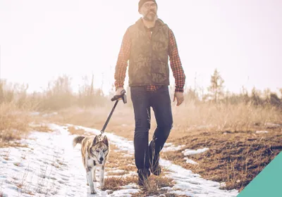 A man walking his dog on a snowy path