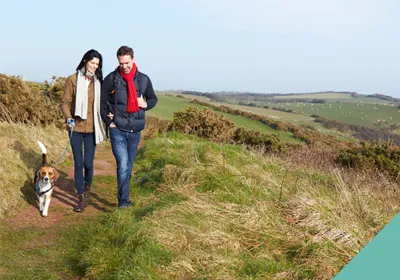 man and woman walking dog in field